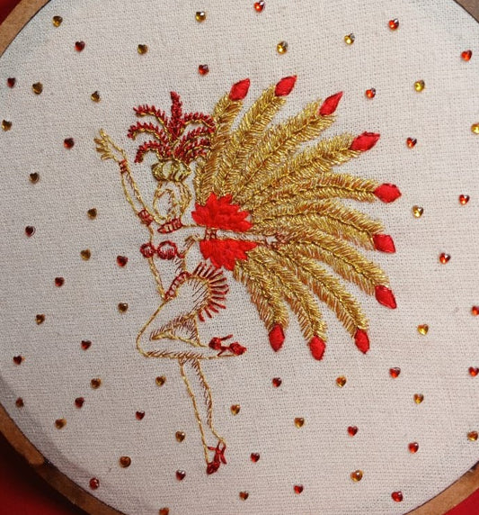 Handmade showgirl embroidery with gold and red feathers, metallic thread, and crystal accents on raw cotton fabric.