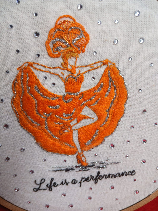Handmade embroidery artwork featuring an orange dancer with crystal accents on raw cotton fabric.